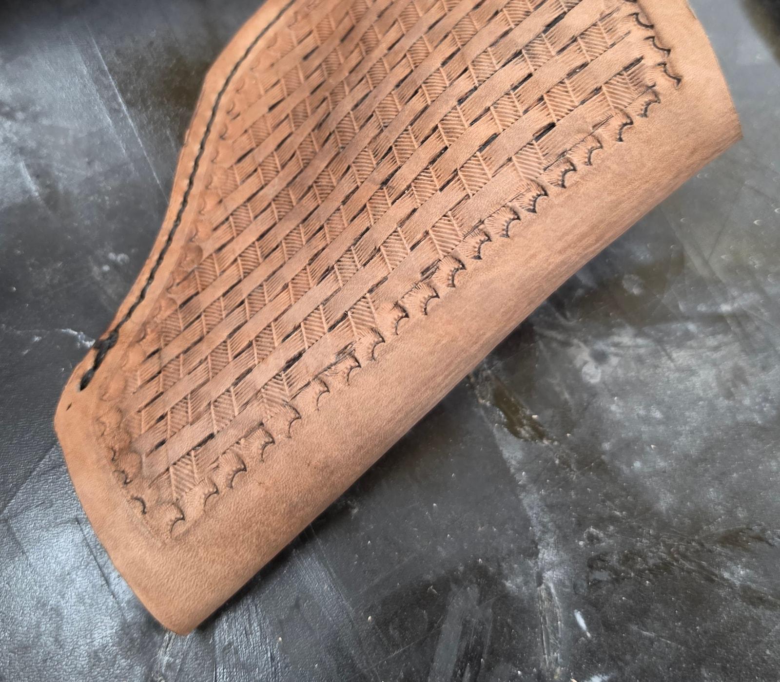 Close detail of basketweave tooling and stitching on a leather piece at the workbench