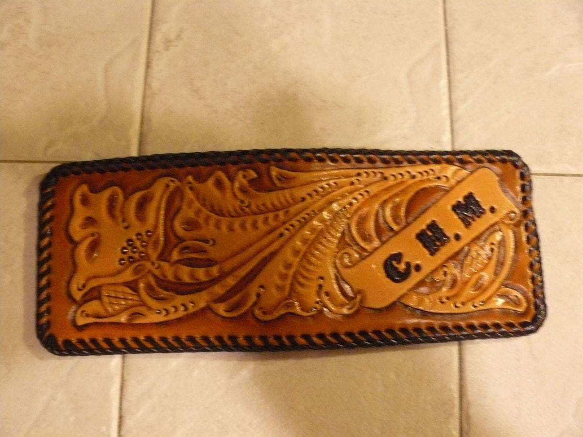 Golden brown leather wallet with floral tooling, laced edges, and C.H.M. initials