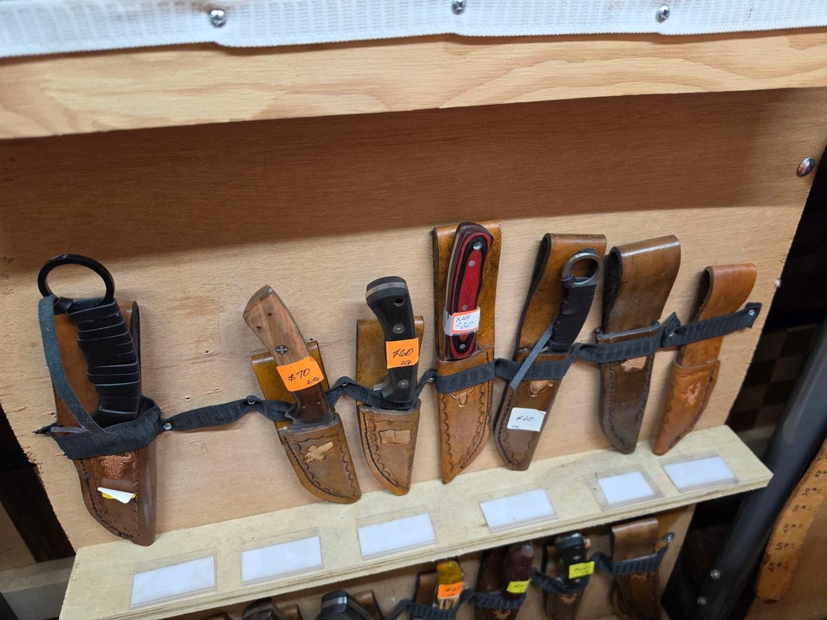 Assorted leather knife sheaths with knives on a wooden shop display