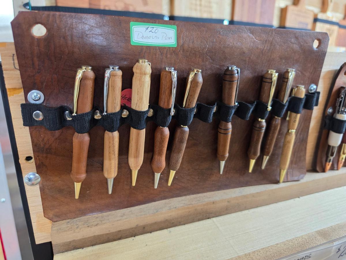 Wooden-barreled pens held in black loops on a leather shop display
