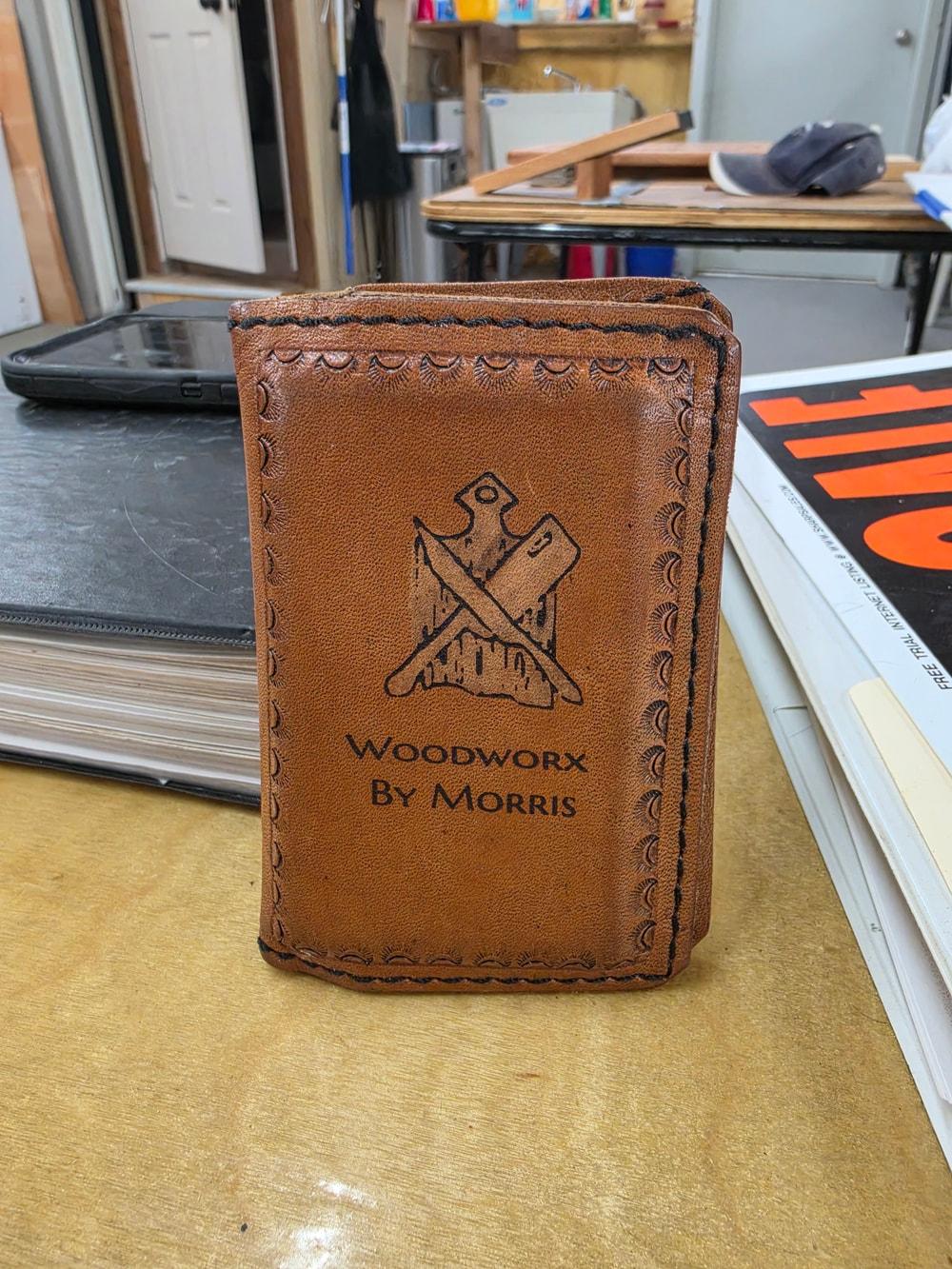A leather piece with a stitched border bearing WoodWorx by Morris lettering and crossed woodworking tools